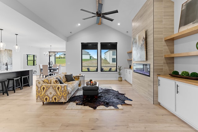 living area featuring high vaulted ceiling, light wood-style flooring, recessed lighting, ceiling fan with notable chandelier, and a fireplace