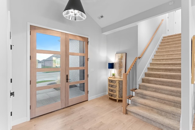 entryway with wood finished floors, visible vents, vaulted ceiling, stairs, and french doors