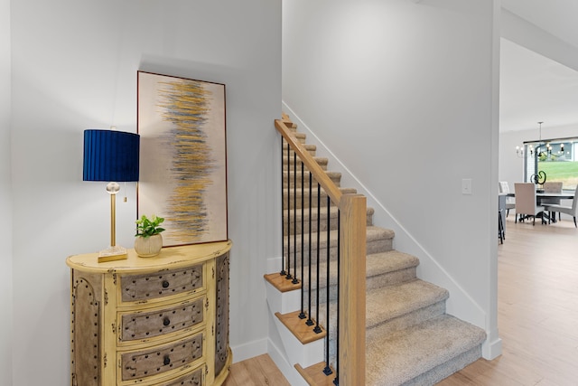 staircase featuring baseboards, wood finished floors, and a notable chandelier