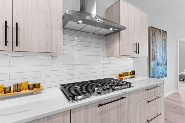 kitchen featuring stainless steel gas cooktop, wall chimney exhaust hood, light brown cabinetry, and modern cabinets