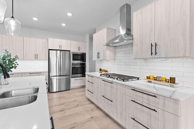 kitchen featuring modern cabinets, stainless steel appliances, light brown cabinetry, wall chimney range hood, and a sink