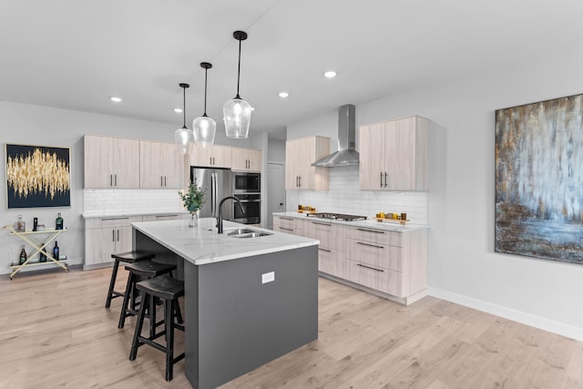 kitchen featuring a center island with sink, appliances with stainless steel finishes, a breakfast bar area, wall chimney range hood, and a sink