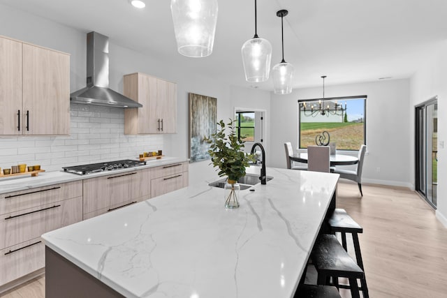 kitchen featuring wall chimney range hood, modern cabinets, stainless steel gas cooktop, and a sink