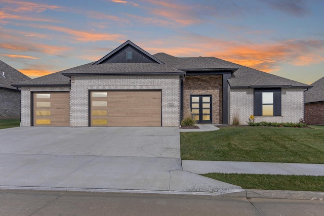 view of front facade featuring driveway, a shingled roof, a lawn, an attached garage, and brick siding