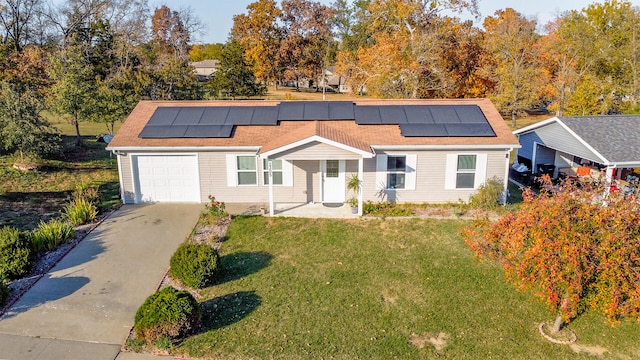 single story home with roof mounted solar panels, an attached garage, concrete driveway, and a front lawn