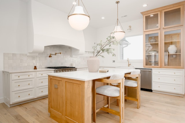 kitchen with appliances with stainless steel finishes, a kitchen island, backsplash, white cabinetry, and light hardwood / wood-style flooring