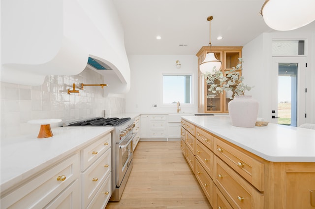 kitchen with high end range, white cabinets, light wood-type flooring, and plenty of natural light