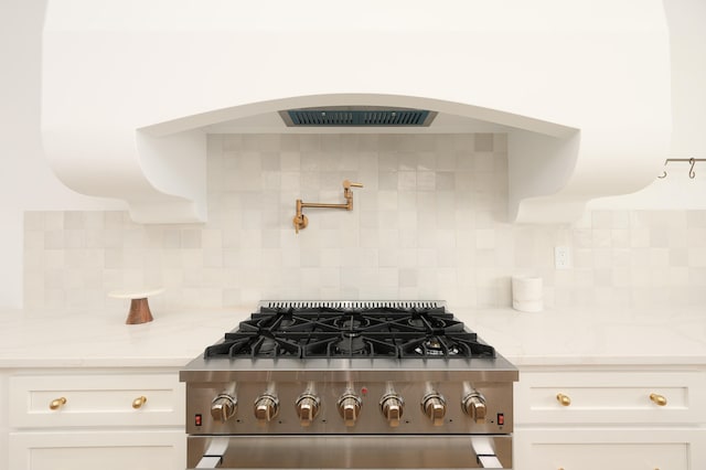 kitchen with white cabinetry, decorative backsplash, light stone countertops, and stainless steel stove