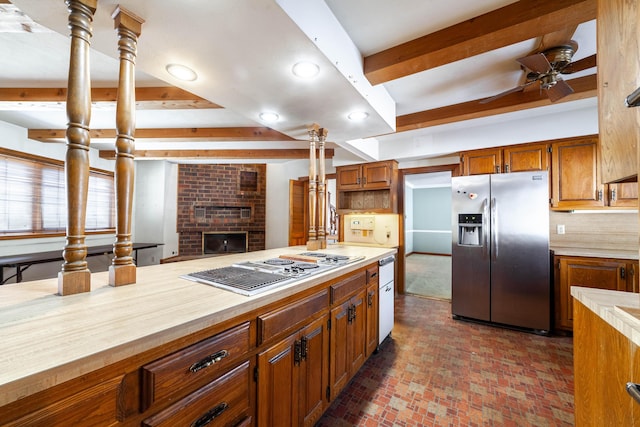 kitchen with ceiling fan, beam ceiling, stainless steel appliances, a brick fireplace, and decorative backsplash