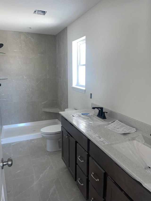 bathroom with vanity, toilet, and a tile shower