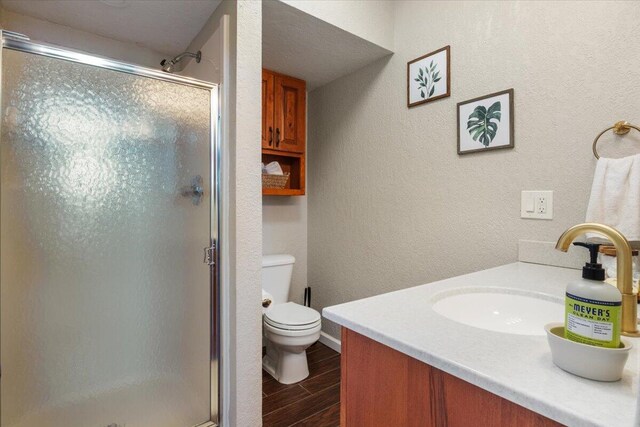 bathroom with a shower with door, vanity, wood-type flooring, and toilet