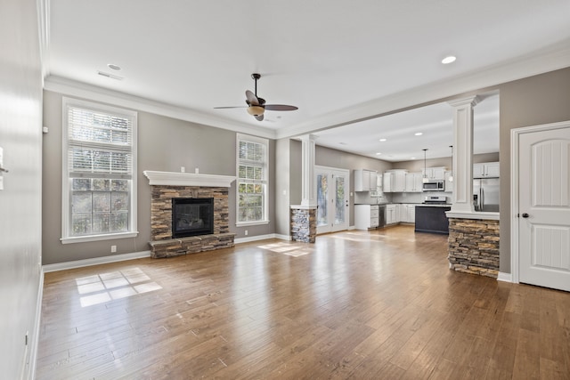 unfurnished living room featuring a fireplace, a wealth of natural light, light wood-type flooring, and decorative columns