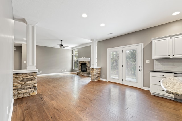 unfurnished living room with hardwood / wood-style floors, a fireplace, ceiling fan, and decorative columns