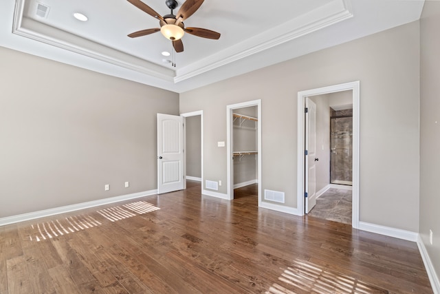 unfurnished bedroom with dark wood-type flooring, ceiling fan, a raised ceiling, and a spacious closet