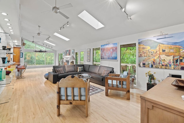 living room with lofted ceiling with skylight, track lighting, light hardwood / wood-style flooring, and ceiling fan