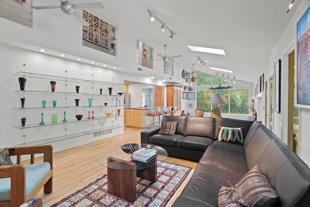 living room featuring ceiling fan, high vaulted ceiling, a skylight, and light wood-type flooring