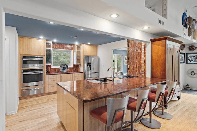 kitchen featuring a large island, a breakfast bar area, dark stone counters, light hardwood / wood-style flooring, and stainless steel appliances