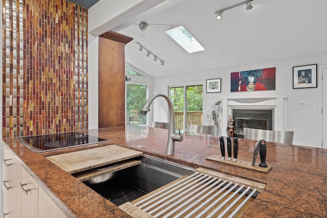 kitchen with black electric stovetop, lofted ceiling with skylight, light brown cabinetry, and rail lighting