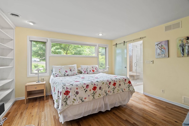 bedroom with light hardwood / wood-style floors, a barn door, and connected bathroom