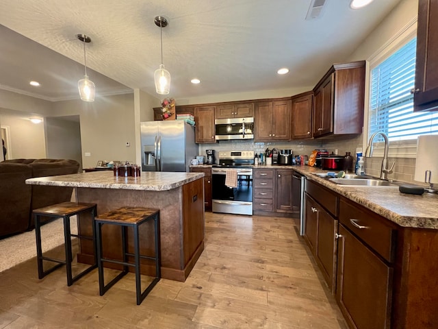 kitchen with stainless steel appliances, sink, decorative light fixtures, light hardwood / wood-style floors, and a kitchen island