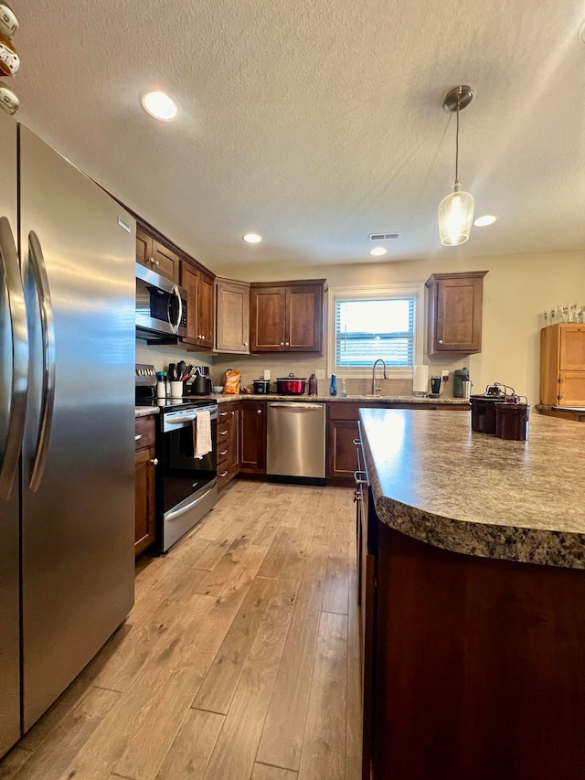 kitchen featuring pendant lighting, sink, a textured ceiling, appliances with stainless steel finishes, and light hardwood / wood-style floors