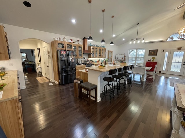 kitchen featuring dark wood-type flooring, a kitchen breakfast bar, an island with sink, black fridge with ice dispenser, and decorative light fixtures