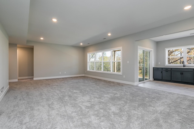 unfurnished living room with light colored carpet, a healthy amount of sunlight, and sink