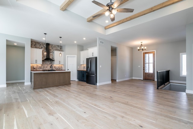 kitchen featuring white cabinets, black refrigerator with ice dispenser, a center island with sink, and wall chimney exhaust hood