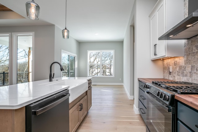 kitchen featuring wall chimney exhaust hood, black gas range oven, sink, pendant lighting, and dishwasher