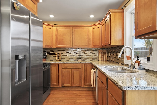 kitchen with light stone counters, sink, light hardwood / wood-style flooring, and appliances with stainless steel finishes