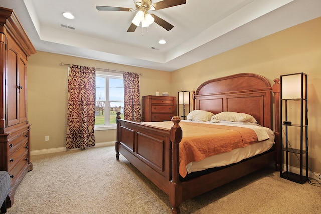 carpeted bedroom with ceiling fan and a raised ceiling