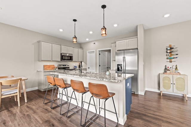 kitchen featuring a kitchen island with sink, appliances with stainless steel finishes, hanging light fixtures, and dark hardwood / wood-style floors