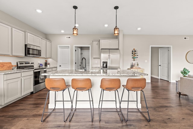 kitchen with dark wood-type flooring, appliances with stainless steel finishes, hanging light fixtures, and a kitchen island with sink