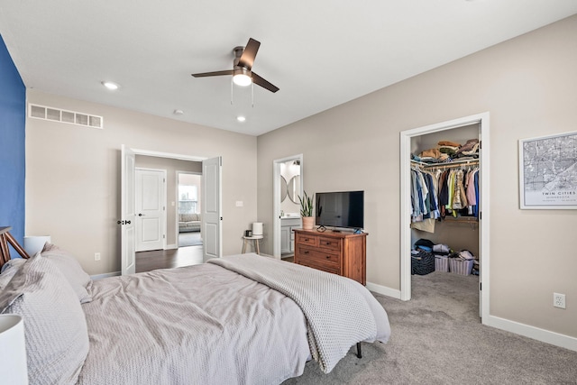 bedroom with ensuite bathroom, ceiling fan, a walk in closet, light colored carpet, and a closet