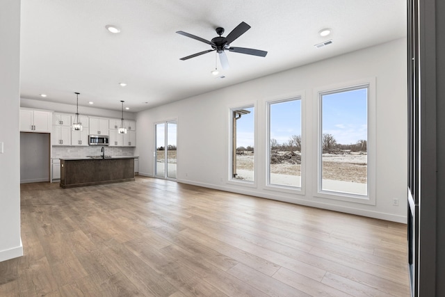 unfurnished living room featuring light wood-type flooring, ceiling fan, and sink