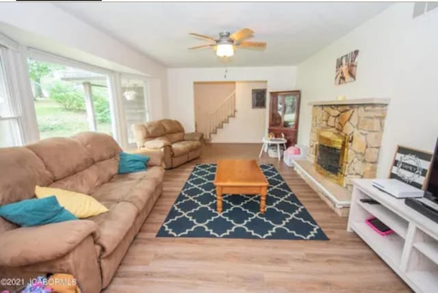 living room with light wood-type flooring, a stone fireplace, and ceiling fan