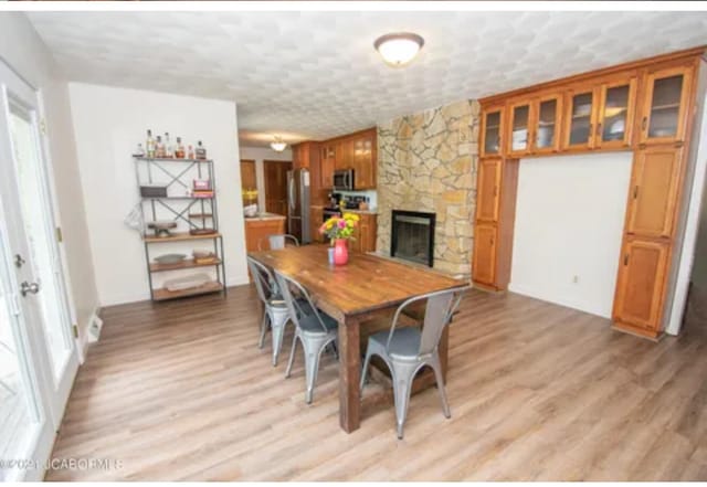 dining space featuring a textured ceiling, light hardwood / wood-style floors, and a stone fireplace