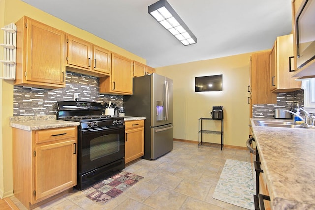 kitchen featuring sink, black gas range, decorative backsplash, and stainless steel fridge