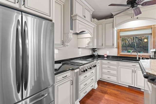 kitchen featuring ceiling fan, dark stone countertops, dark wood-type flooring, sink, and stainless steel appliances