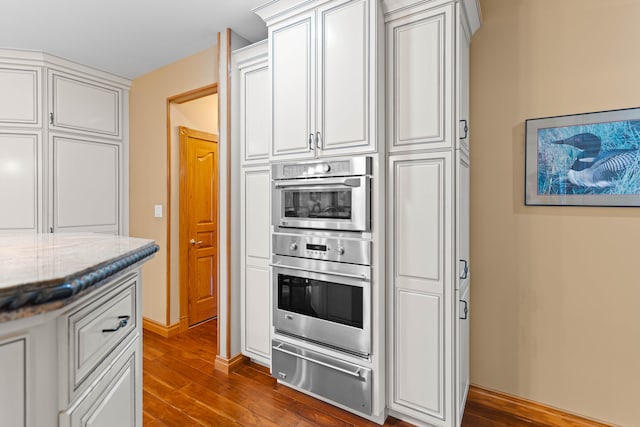 kitchen with hardwood / wood-style floors, double oven, white cabinetry, and light stone counters