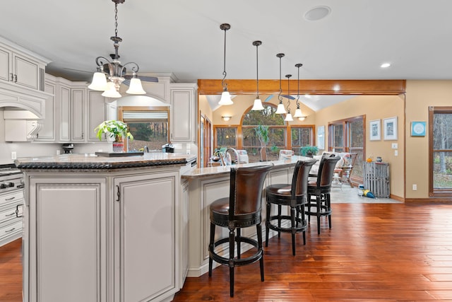 kitchen featuring beam ceiling, a kitchen island with sink, dark hardwood / wood-style floors, pendant lighting, and light stone counters