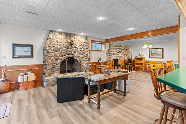 living room with hardwood / wood-style flooring, a stone fireplace, and a drop ceiling