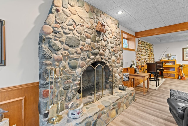 living room featuring a stone fireplace, a drop ceiling, and hardwood / wood-style flooring