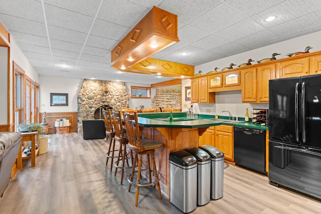 kitchen featuring black appliances, sink, light wood-type flooring, a stone fireplace, and a kitchen breakfast bar