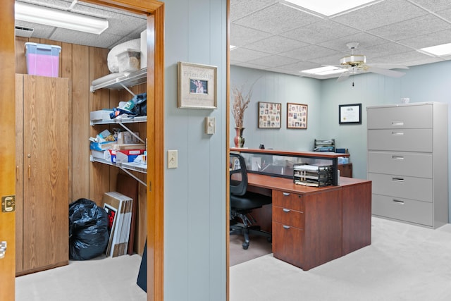 carpeted home office featuring wood walls and ceiling fan