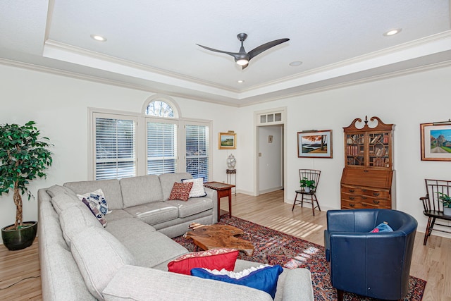 living room with a raised ceiling, crown molding, ceiling fan, and light wood-type flooring