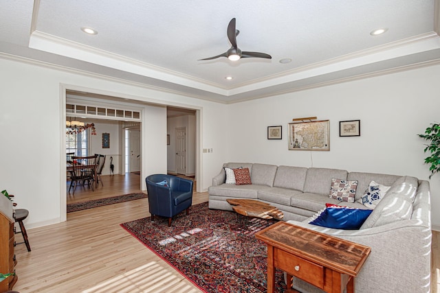 living room featuring ceiling fan, a raised ceiling, crown molding, a textured ceiling, and light wood-type flooring