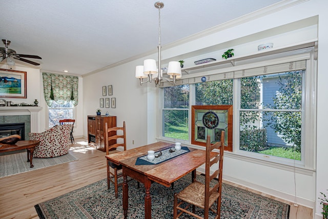 dining space with hardwood / wood-style flooring, ceiling fan with notable chandelier, ornamental molding, and a tile fireplace