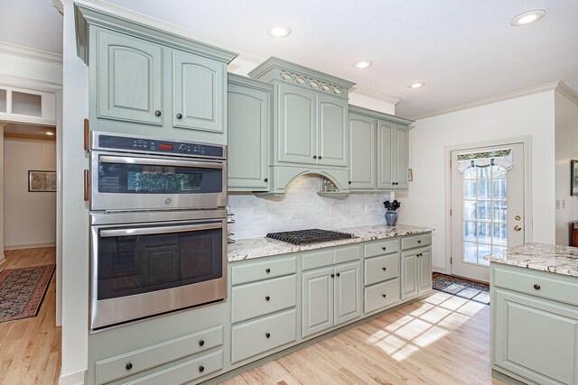 kitchen with appliances with stainless steel finishes, tasteful backsplash, light stone counters, ornamental molding, and light hardwood / wood-style flooring