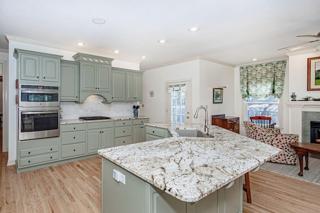 kitchen with stainless steel double oven, an island with sink, a healthy amount of sunlight, and sink